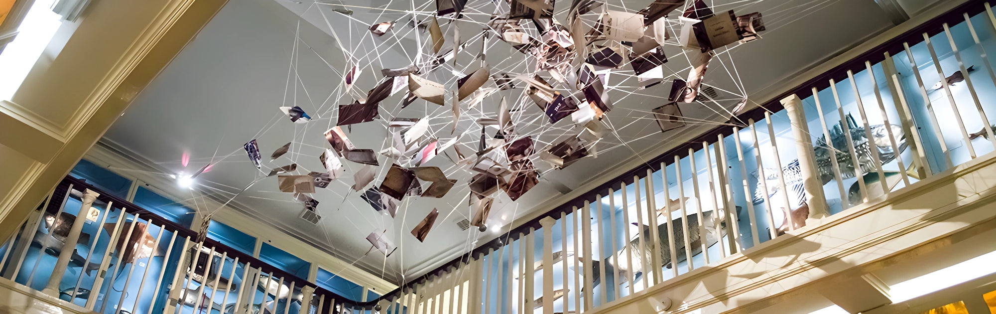 Modern chandelier hanging from a high ceiling in a building with large windows.