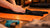A person's hands are smoothing out a black t-shirt laid flat on an orange perforated mat over a worktable.