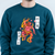 A person wearing a dark teal custom sweatshirt with a graphic of a pink and orange demon character surrounded by flames, with Japanese text on white labels.