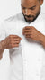 A close-up of a man wearing a white chef jacket, adjusting the front buttons with both hands against a plain white background.