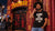 A man with an afro stands in front of a red and black 'Zanzibar' bar storefront at night, wearing a black graphic organic T-shirt that reads 'NO MUSIC ON A DEAD PLANET' and blue jeans.