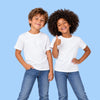 Two children, a boy and a girl, standing side-by-side against a solid light blue background. Both are wearing blank white crewneck t-shirts and blue jeans, smiling and posing for the camera.